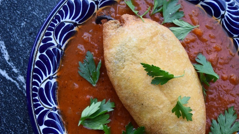 A blue dish filled with a red tomato sauce and topped with a fried chile and parsley leaves