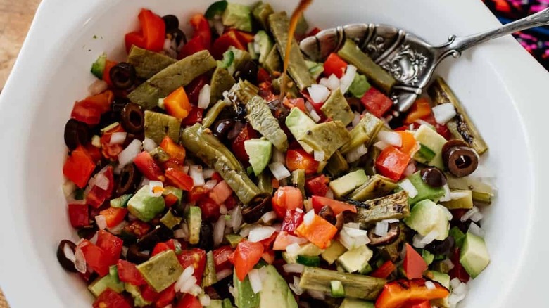 In a white bowl a salad of cactus, tomatoes, olives, onions, and peppers