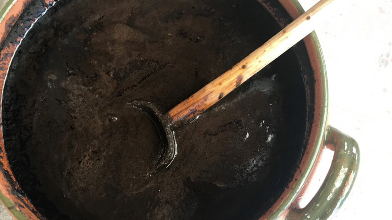 A pot of thick black mole sauce stirred with a wooden spoon