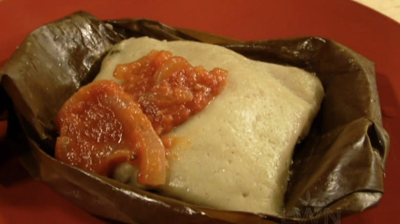 A close-up of tamal in an opened banana leaf and topped with a sauce
