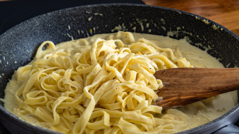 Fettuccine being stirred in a pan with a wooden spoon