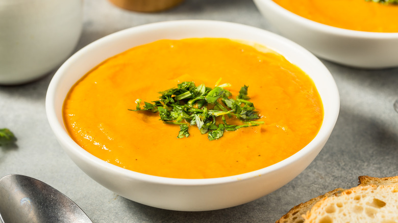White bowl of carrot soup with herbs on top