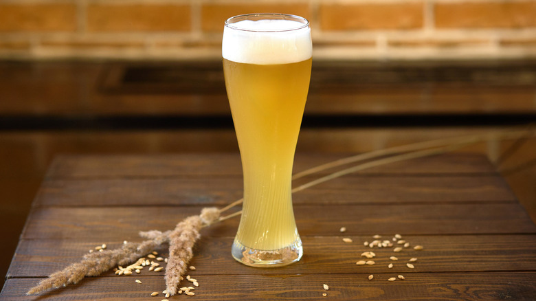 A tall glass of hefeweizen on a table with some wheat stalks