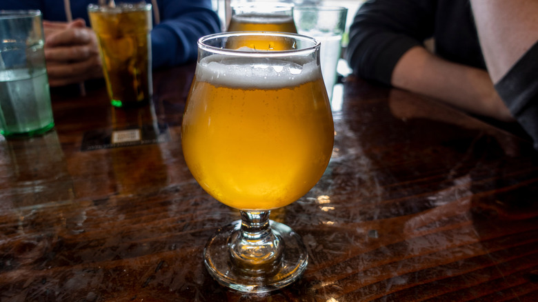 A farmhouse beer on a table with bar patrons in the background