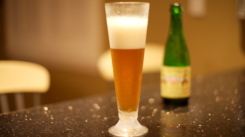 A sour beer in a pilsner glass with the bottle in the background