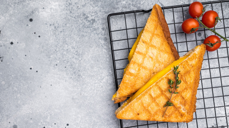 Top view of halved grilled cheese sandwich on wire rack garnished with fresh thyme sprig alongside cherry tomatoes