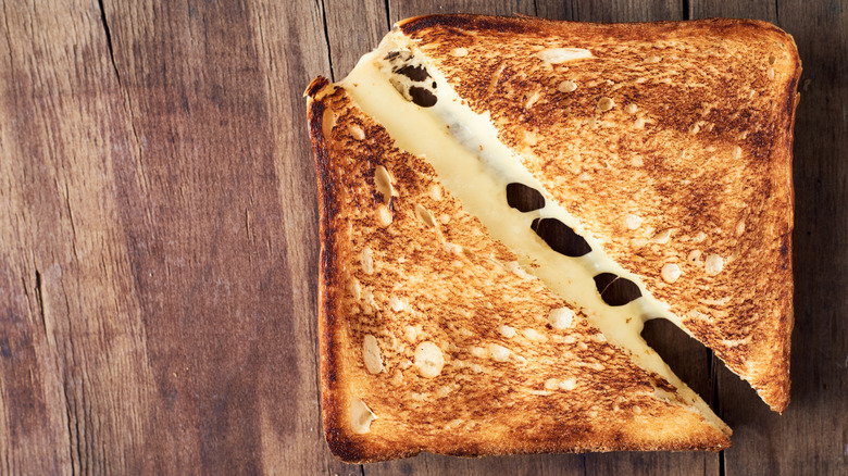 Halved grilled cheese sandwich with cheese pull on wooden cutting board