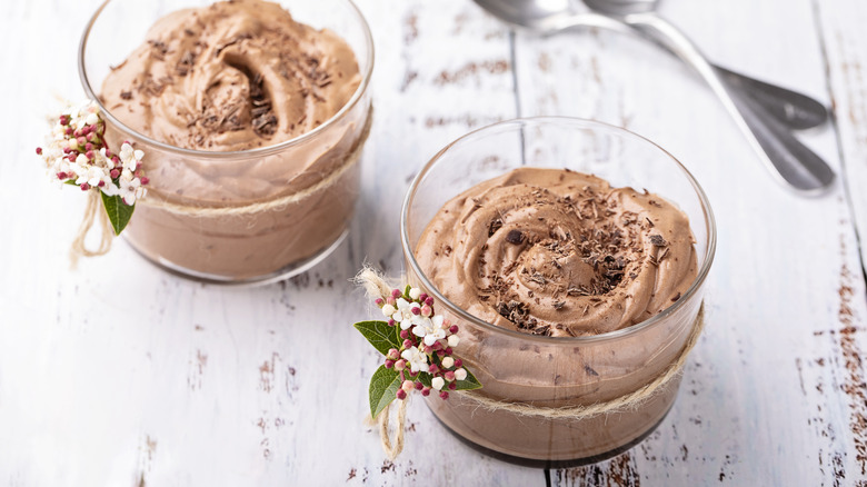 Two glass cups filled with chocolate mousse and decorated with small flowers