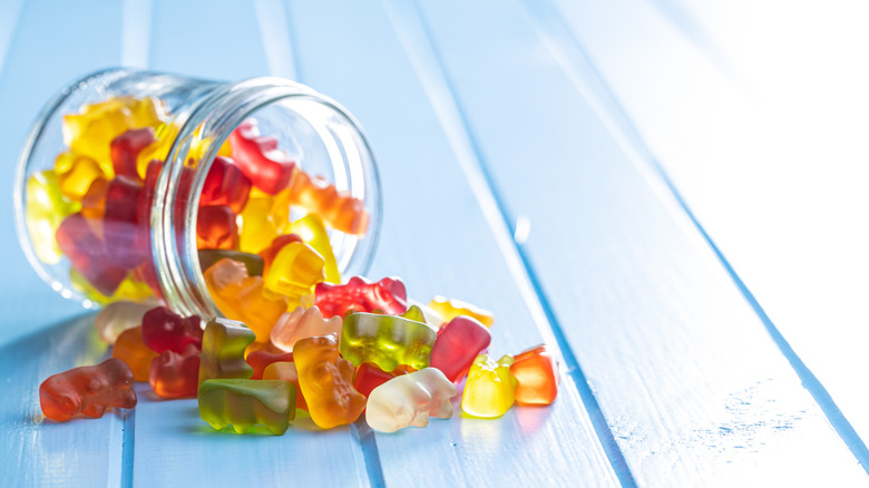 Different flavored gummy bears spilling out of a jar.