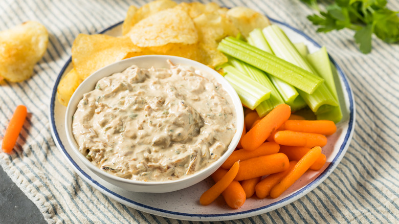 Onion dip in a white bowl with carrots, celery, and potato chips on a round white plate