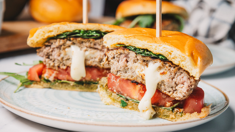 A pesto turkey burger cut in half with mozzarella oozing out.