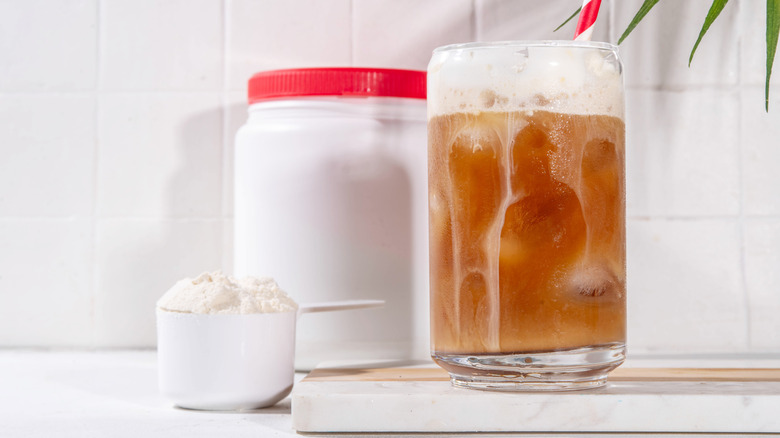 Protein powder container and scoop alongside an iced coffee