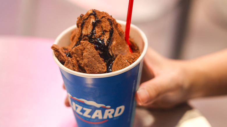 Person holding Dairy Queen cup with soft serve, Biscoff cookie pieces, fudge sauce on top