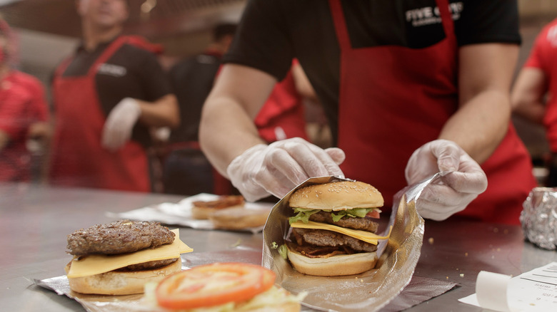 A Five Guys employee wrapping a burger in foil with other employees behind