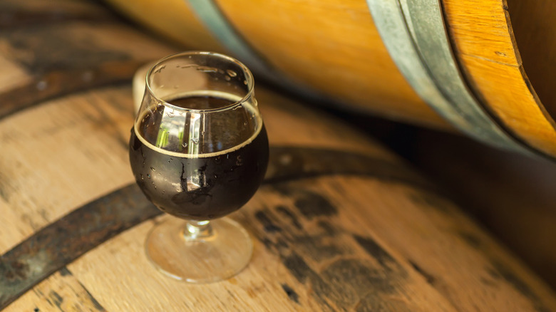 A glass of dark beer balanced on a wooden barrel.