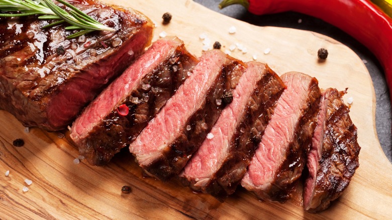Grilled steak cut into slices on wood board