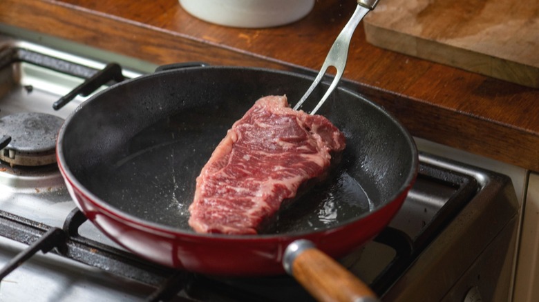 Person placing raw steak into pan in home kitchen