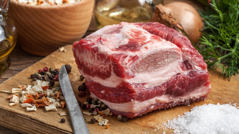 A large chunk of raw, well-marbled brisket on a wooden cutting board beside a pile of salt
