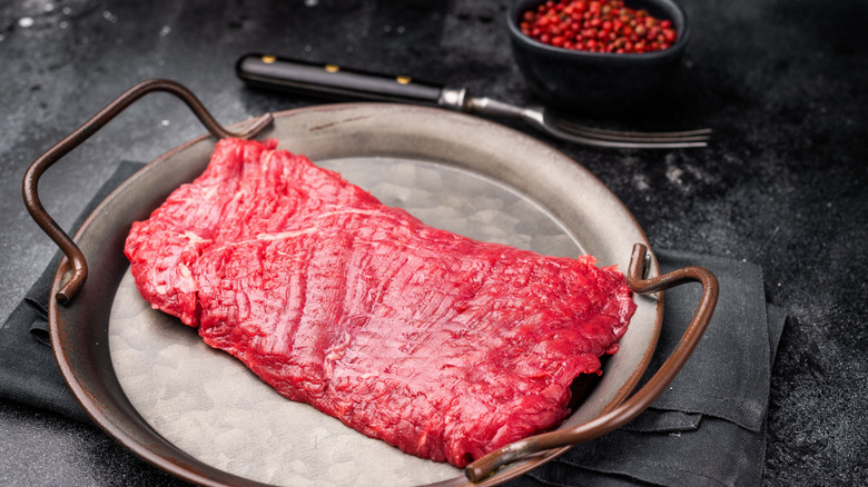 An uncooked piece of raw flank steak on a metal plate with handles on it