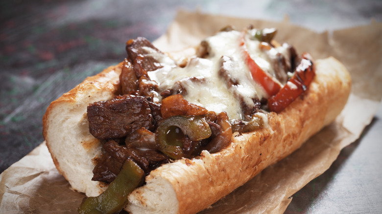 A cheesesteak with green and red peppers on a piece of parchment paper