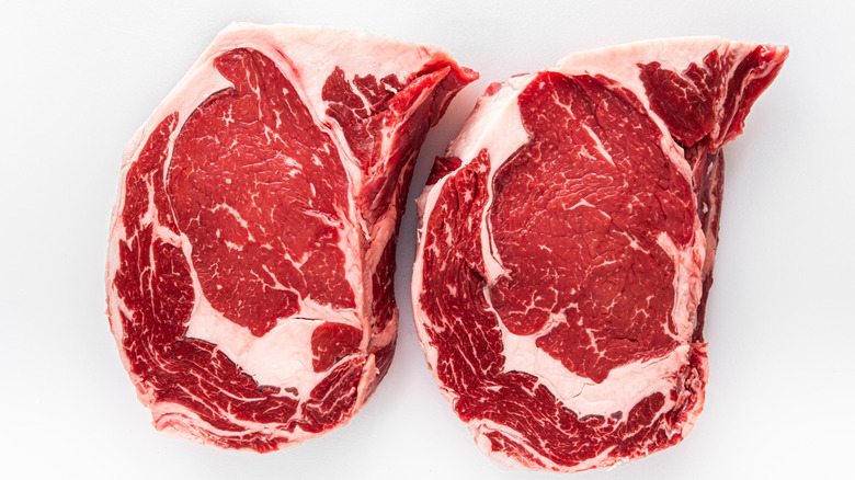 Two raw ribeye steaks beside one another on a white surface