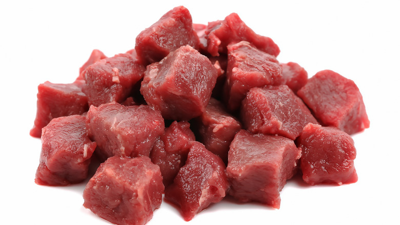 A pile of cubed raw stew meat on a white background