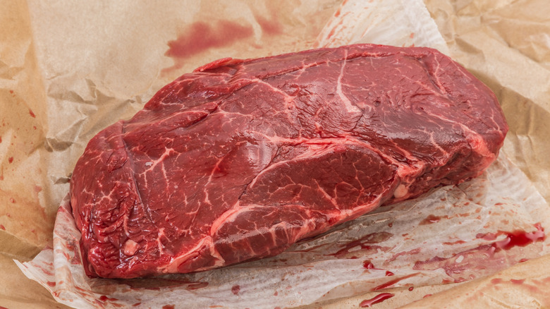 A raw piece of top sirloin laying on a large piece of parchment paper with myoglobin on it