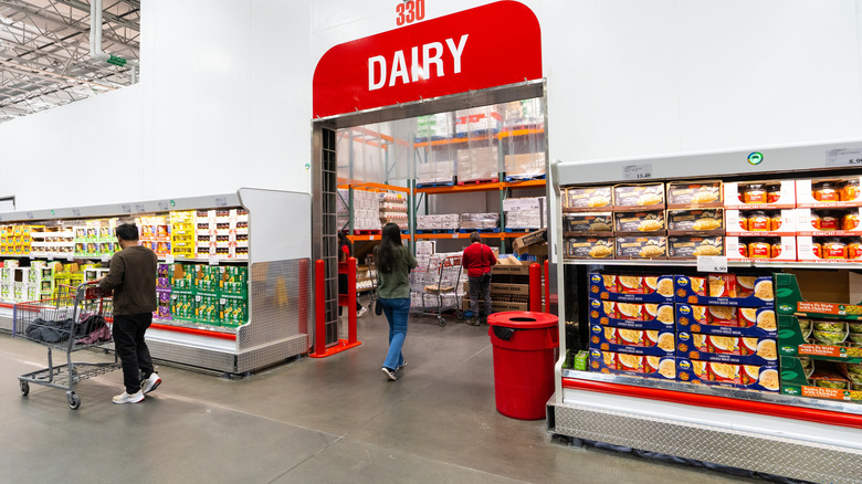 The dairy fridges inside a Costco with shoppers walking around.
