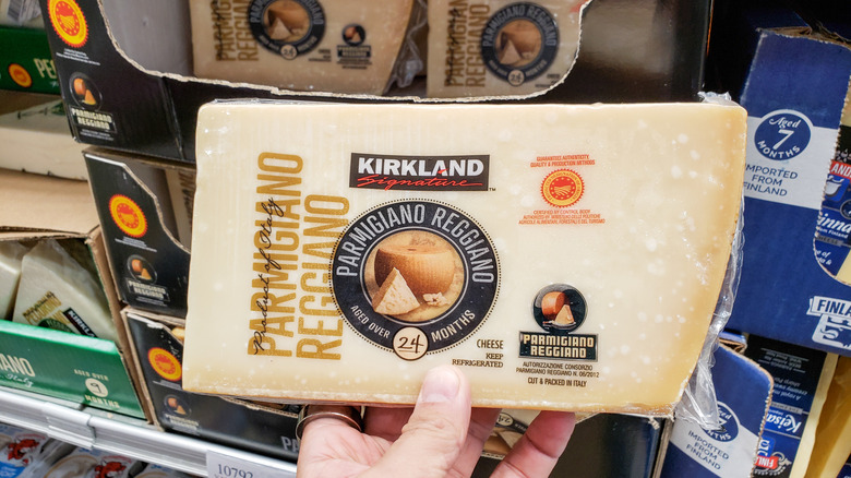 A hand holding a package of Costco's 24-month aged Parmesan in front of a shelf of more packages