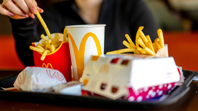 A woman picking up a french fry from a box sitting on a black plastic tray full of McDonald's food.