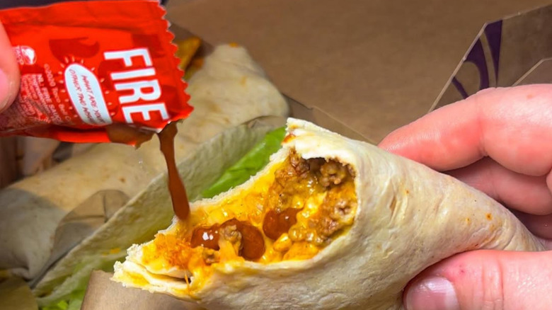 A person pours Fire sauce over a Taco Bell burrito