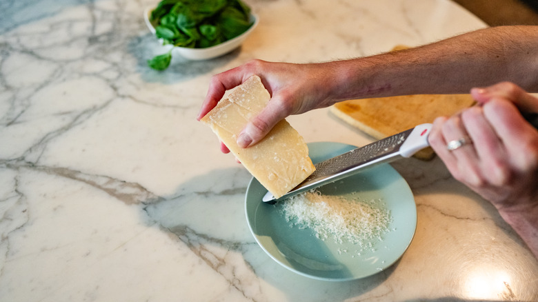 Hands grating parmesan into a bowl