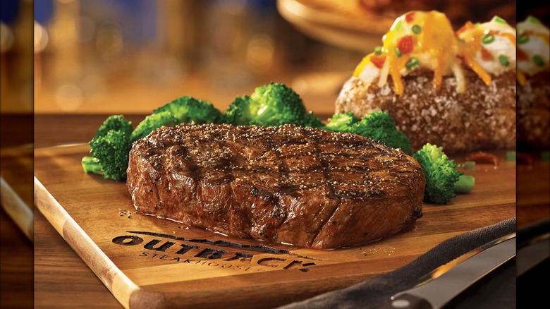 The Down Under Delmonico Ribeye from Outback Steakhouse in front of pieces of broccoli and a loaded baked potato