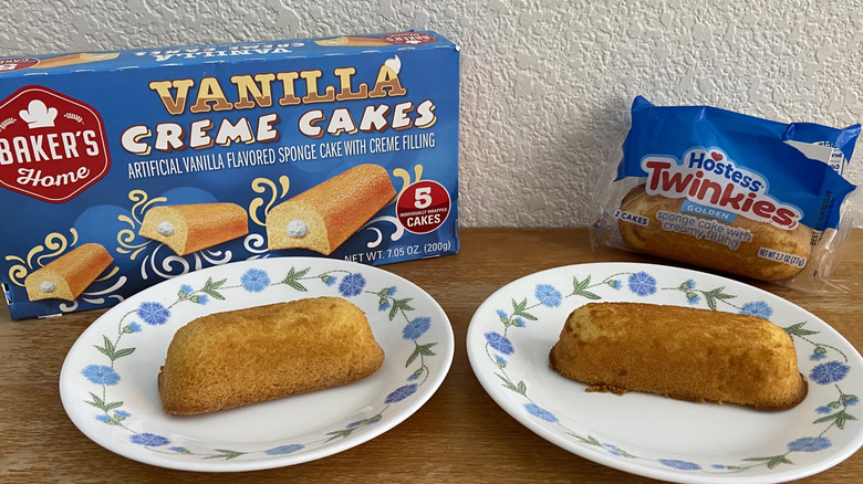 A Baker's Home Vanilla Creme Cake and a Twinkie, each on a plate in front of its packaging