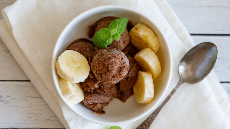 A bowl of chocolate ice cream topped with mint and banana slices