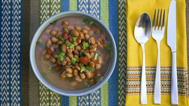 A bowl of charro beans on a patterned tablecloth.