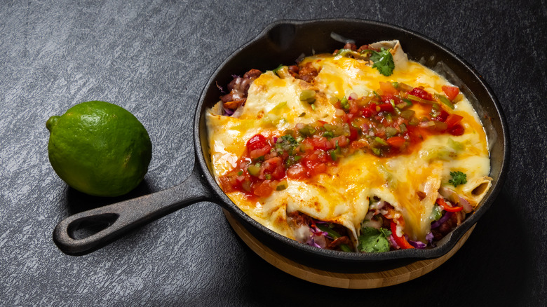 Enchiladas in a cast iron skillet next to a lime.