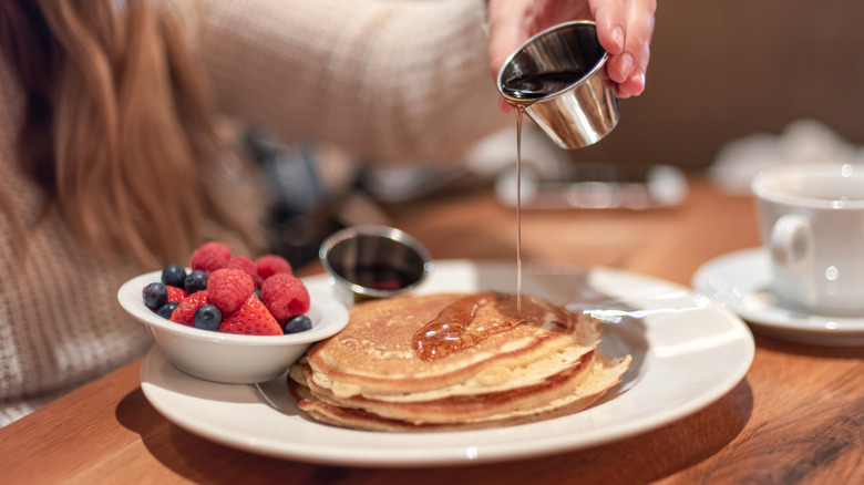 Close up of a woman's hands pouring syrup on a pile of pancakes