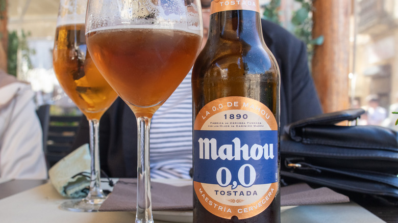 A bottle of Mahou 0.0 beer sitting on a table next to a glass of the beer.