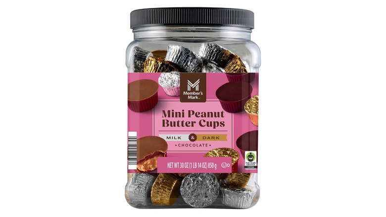 A large, clear plastic tub with a pink Member's Mark label full of gold and silver foil wrapped peanut butter cups on a white background.