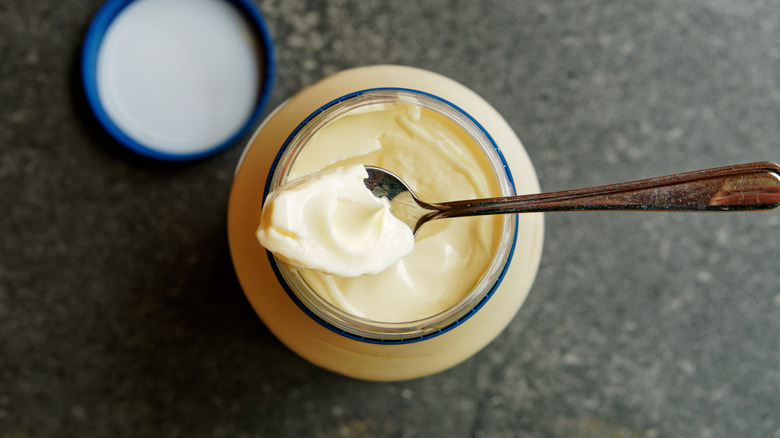 Top view of an open jar of store-bought mayonnaise with a spoonful of mayo on top