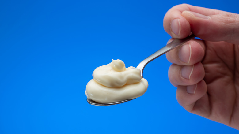 Hand holding spoonful of mayo against blue background