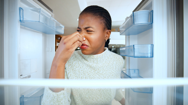 Woman pinching her nose in disgust while standing in front of an open refrigerator