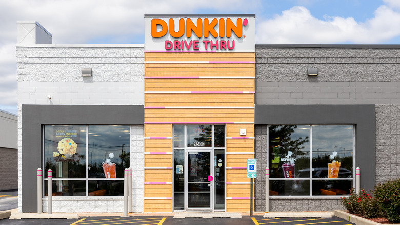 The front of a Dunkin' drive-thru location with a blue sky and fluffy clouds in the background
