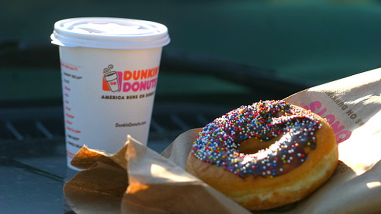 A Dunkin' to-go coffee cup next to a donut on a paper bag