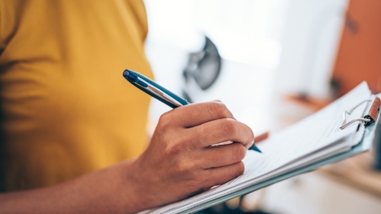 A person holding a clipboard and pen, possibly taking inventory.