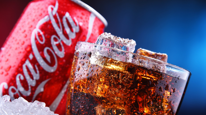 Coca-Cola can and soda-filled glass on crushed ice