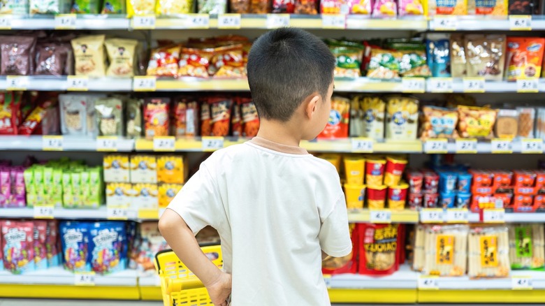 A child standing in the snack aisle of a supermarket.