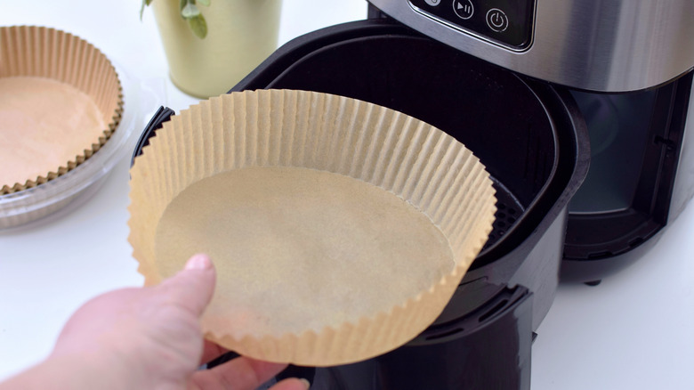 hand putting a brown paper liner into an air fryer