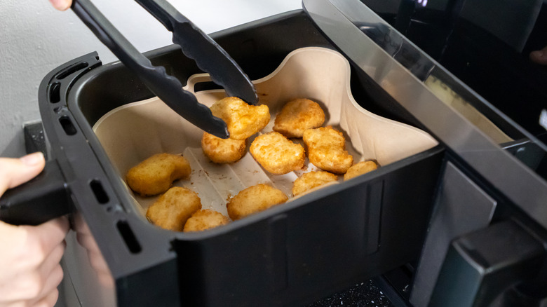 black tongs being used to remove chicken nuggets from a black air fryer